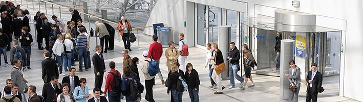 Menschen betreten und verlassen durch mehrere Drehtüren die Glashalle der Leipziger Messe; im lichtdurchfluteten Eingangsbereich herrscht reger Besucherverkehr. Menschen betreten und verlassen durch mehrere Drehtüren die Glashalle der Leipziger Messe; im lichtdurchfluteten Eingangsbereich herrscht reger Besucherverkehr.