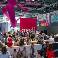 Viele Messebesucherinnen und -besucher versammeln sich am farbenfrohen Stand von medi auf der OTWorld, über dem eine große pinke Skulptur schwebt