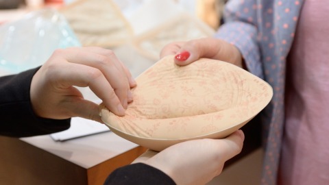 Two people are holding a soft, skin-colored breast prosthesis with a floral pattern together in their hands.