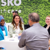Conversation situation at the trade fair stand: six people laughing at each other.