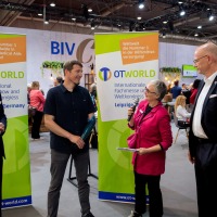 A female person with a microphone interviews a male person with a prosthetic forearm.