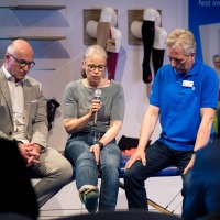A woman with a microphone sits between two men and talks about compression stockings.