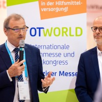 Two men stand in front of a roll-up display showing the OTWorld logo.