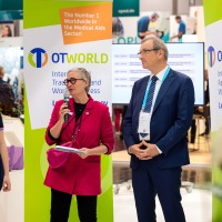 Four people at an official speech at OTWorld, a woman with a microphone speaks, next to her two men in suits and a young woman with a prosthesis.