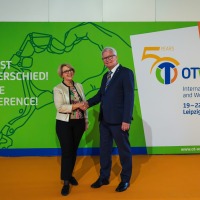Two people shake hands in front of a wall with the OTWorld logo and the slogan “You make the difference!” - Announcing the 2026 trade fair in Leipzig from May 19-22, 2026.