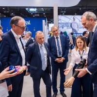 Trade fair visitors in suits look at a modern arm prosthesis presented by exhibitors.