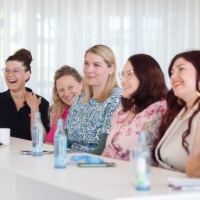 Group of six participants sitting smiling at a conference table, with water bottles and notes in front of them.