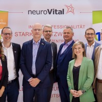 Group photo of nine professionals in front of the OTWorld and neuroVital banners, smiling and in business attire.