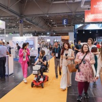 Group of visitors moving between exhibitor stands, including one person on an e-scooter