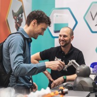 A trade fair visitor tests a technical assistance system at the exhibition stand while an exhibitor watches with a smile.