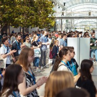 Large crowd in the glass hall, many young visitors wearing trade fair passes and moving around the room.