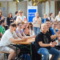 Many young people sit at a table applauding and laughing.