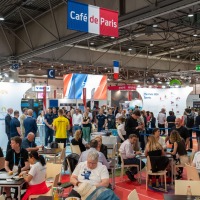 Lots of people at tables, talking, eating and drinking. Above the scene, a banner with the inscription Café de Paris.