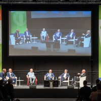 Panel discussion at OTWorld with seven experts on stage, their conversation displayed on a large screen, surrounded by OTWorld banners.