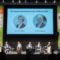 Panel discussion at OT-World with seven experts on stage, their conversation displayed on a large screen, surrounded by OT-World banners.