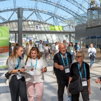 Group of visitors with lanyards walk through the glass hall of the Leipzig Trade Fair, next to a sign with the motto 'You make the difference!