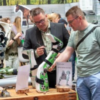 Two men examining child-friendly orthoses with soccer motifs at an exhibition booth with a green backdrop at OTWorld.