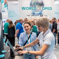 Two women looking at a laptop together. In the background, trade fair activities.