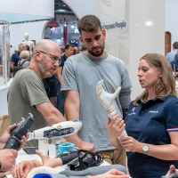 Exhibitor demonstrates a modern hand prosthesis at OTWorld while several visitors listen attentively and examine other prosthetic models.