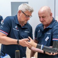 Exhibitor demonstrates a modern hand prosthesis at OT-World while several visitors listen attentively and examine other prosthetic models.
