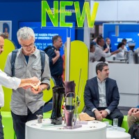 Two men examining new prosthetic components at a display table at OTWorld, with a glowing ‘NEW’ sign above.
