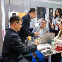 Business meeting at an OTWorld trade fair booth, with five people intently discussing documents and color samples around a small table