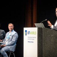 Expert presentation at OTWorld in Leipzig – a speaker presents at the podium while two other professionals listen attentively.