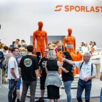 There is a lot of activity at the SPORLASTIC booth – visitors and professionals engage in conversations and examine bright orange demonstration models for orthopaedic applications.