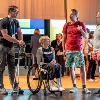 Four visitors with mobility aids and prostheses engage in conversation in a relaxed atmosphere at OTWorld.